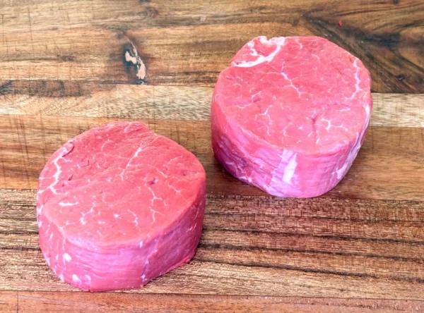 Two raw filet mignon steaks on cutting board